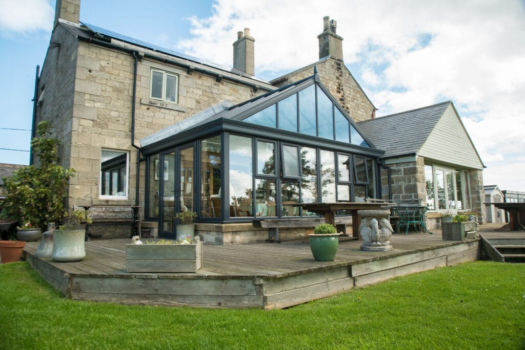 A large glass conservatory surrounded by a patio and a lush garden, showcasing vibrant plants and outdoor seating.