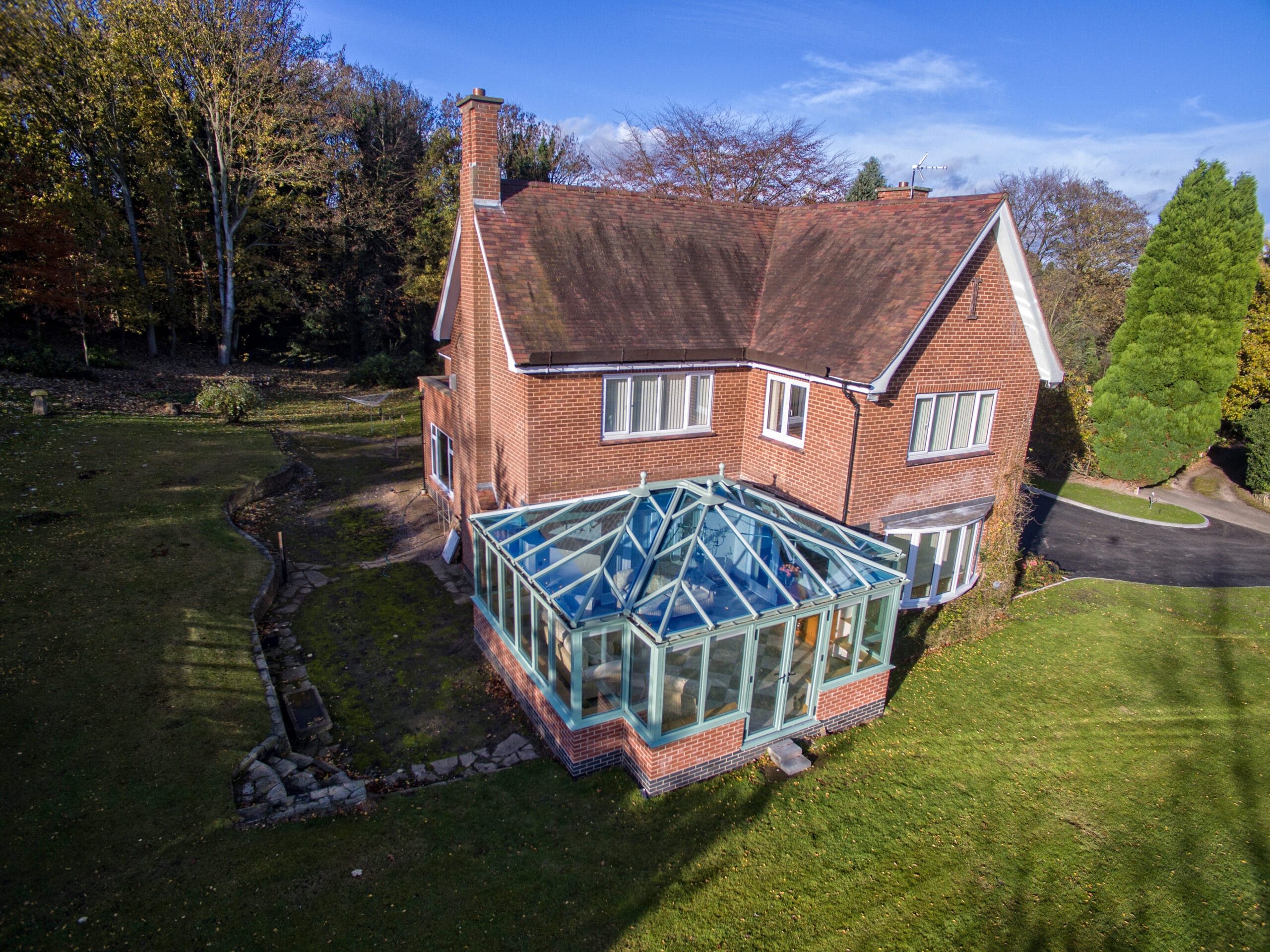 A house featuring a T-shaped conservatory with a glass roof, surrounded by a spacious garden.
